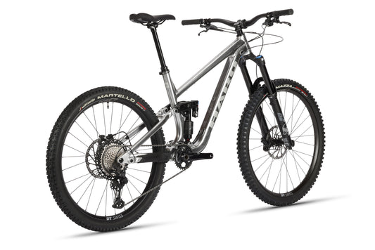 The Greer Alloy LTD 2 by Haro Bikes is a silver mountain bike featuring a robust Haro Greer Alloy frame, large thick tires, an intricate gear system, and a Fox Suspension fork. It’s showcased on a plain white background, emphasizing its rugged durability and sleek design.