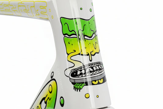 Close-up of a Haro Bikes Rivette Carbon LTD frame featuring vibrant graffiti-style artwork by Mark Ward. The design includes green and yellow drips, stylized faces, and the word HARO on a round emblem, all set against a white background. This limited-edition piece truly stands out.