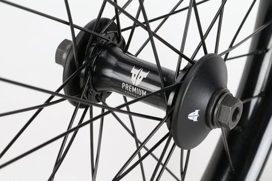 Close-up of a Curb Cutter Front Wheel with black spokes and a Premium hub labeled Varanyak-Felge. The evenly arranged metal spokes encircle the Team-Nabe hub, displaying a small logo on its sides.