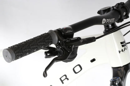 Close-up of bicycle handlebars with a black textured grip, Shimano Deore shifter, and brake lever. The white Double Peak Comp 27.5 frame from Haro Bikes partially shows the brand name in black text.