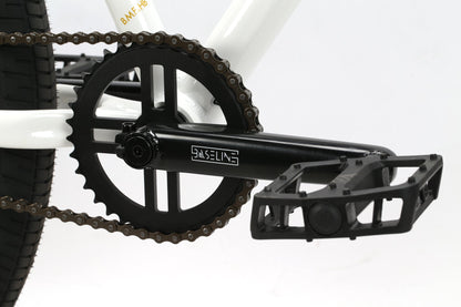 Close-up of a black BMX pedal and chainring with Baseline on the crank arm, mounted on a white Haro Bikes B.M.F frame.