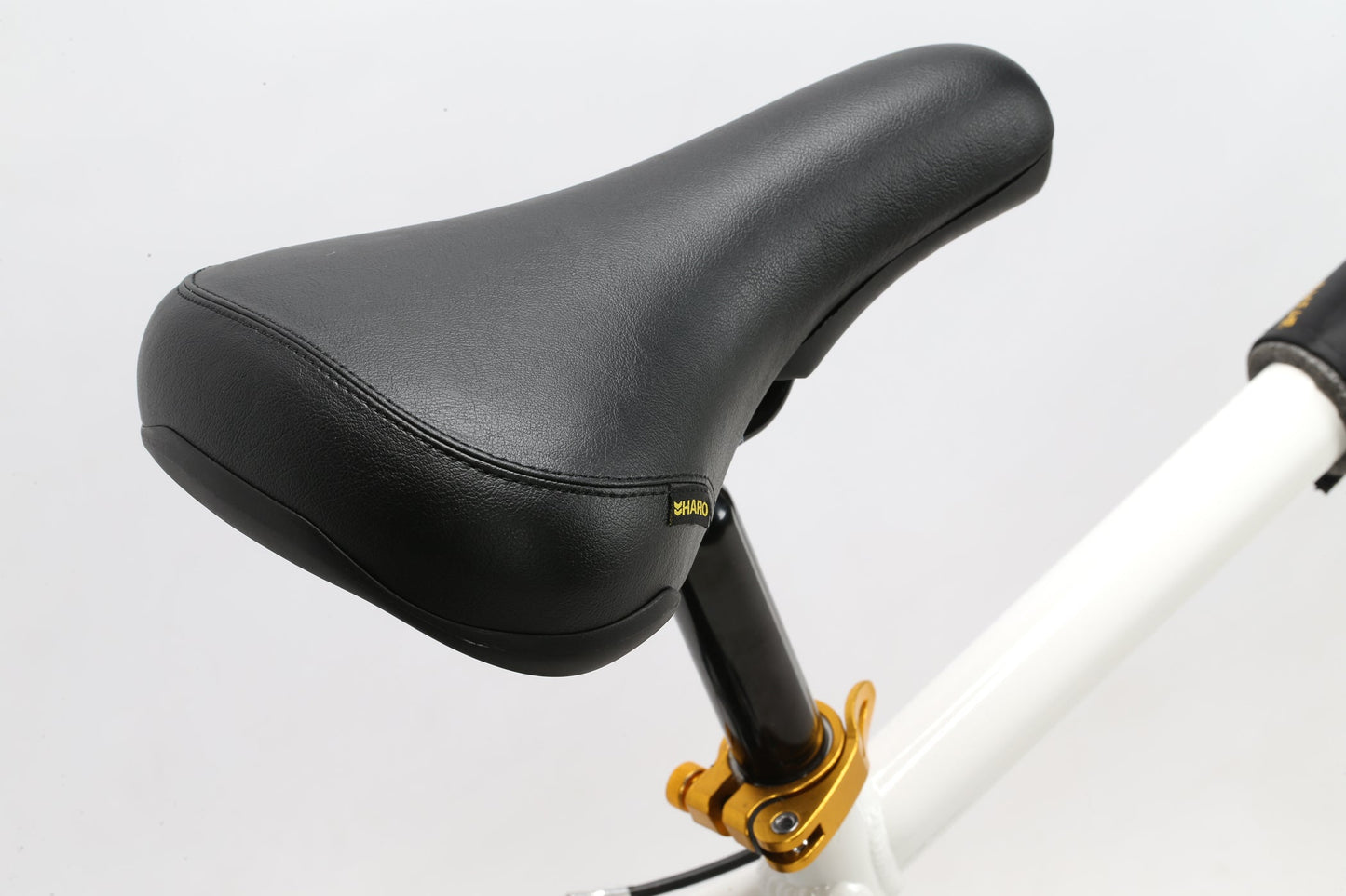 Close-up of a black B.M.F seat on a Haro Bikes white frame with gold highlights, featuring premium BMX components against a plain backdrop.