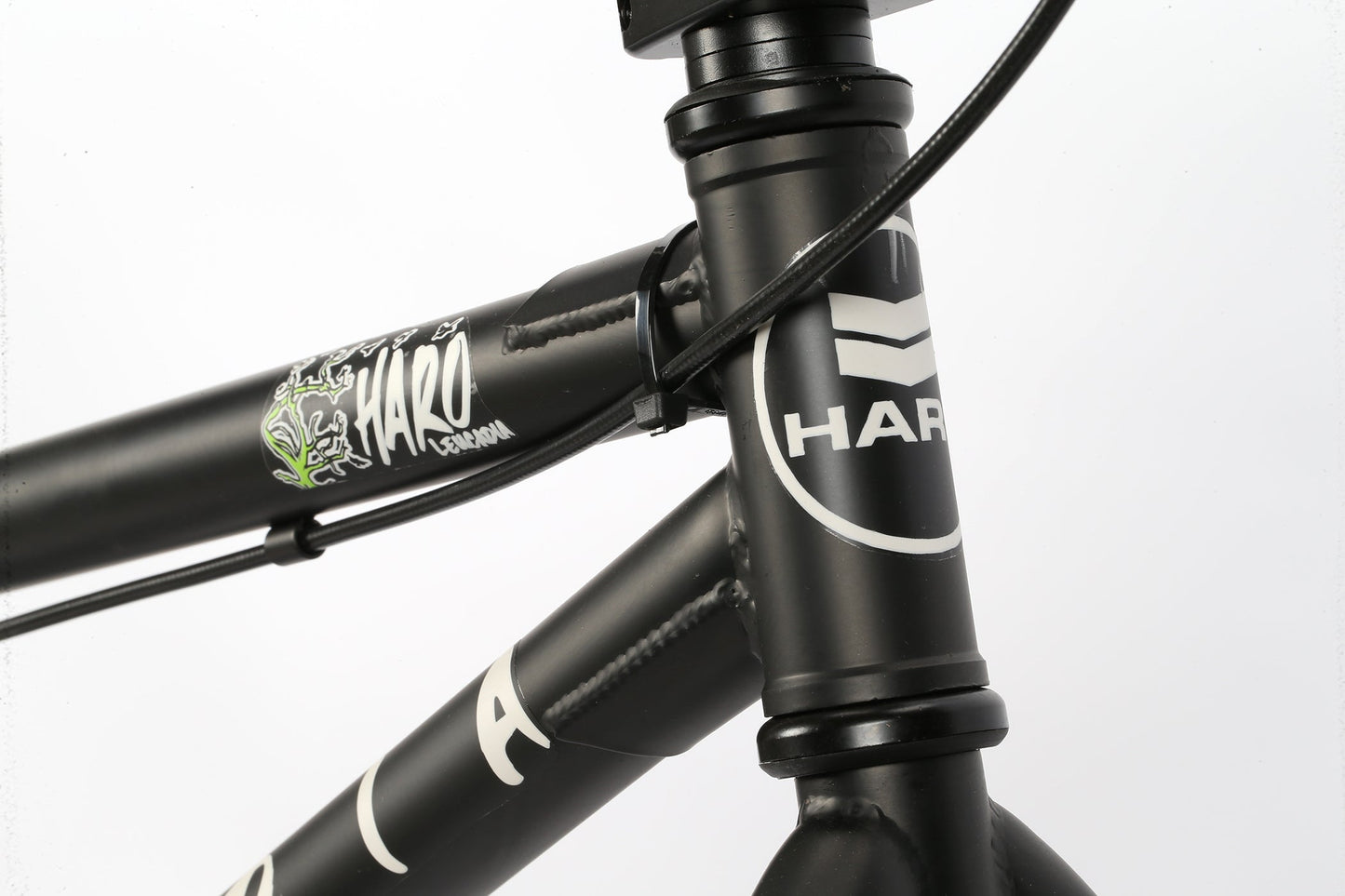 Close-up of the Haro Bikes Leucadia featuring a robust black BMX frame with white graphics and cables on the Hi-Ten-Stahlrahmen top tube.