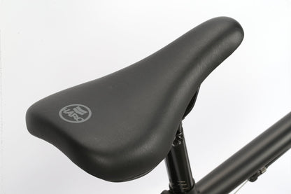 Close-up of a robust black bicycle seat with a logo, attached to a Leucadia BMX Bike by Haro Bikes against a white background.