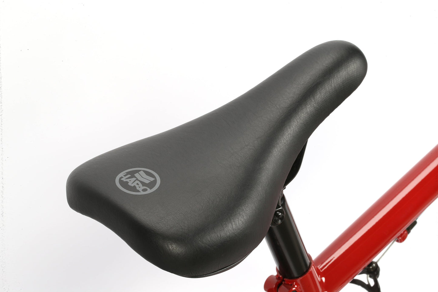 Close-up of a sturdy black Leucadia bike seat with a logo on a red Haro Bikes BMX frame against a white background.