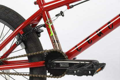 Close-up of Haro Bikes Leucadia BMX bike in red, featuring a chain, crankset, rear brake, and green accents on the Hi-Ten-Stahlrahmen seat post.