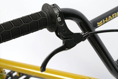 Close-up of Leucadias black brake lever and textured grip on a Haro BMX, featuring its stylish yellow and black frame in the back.