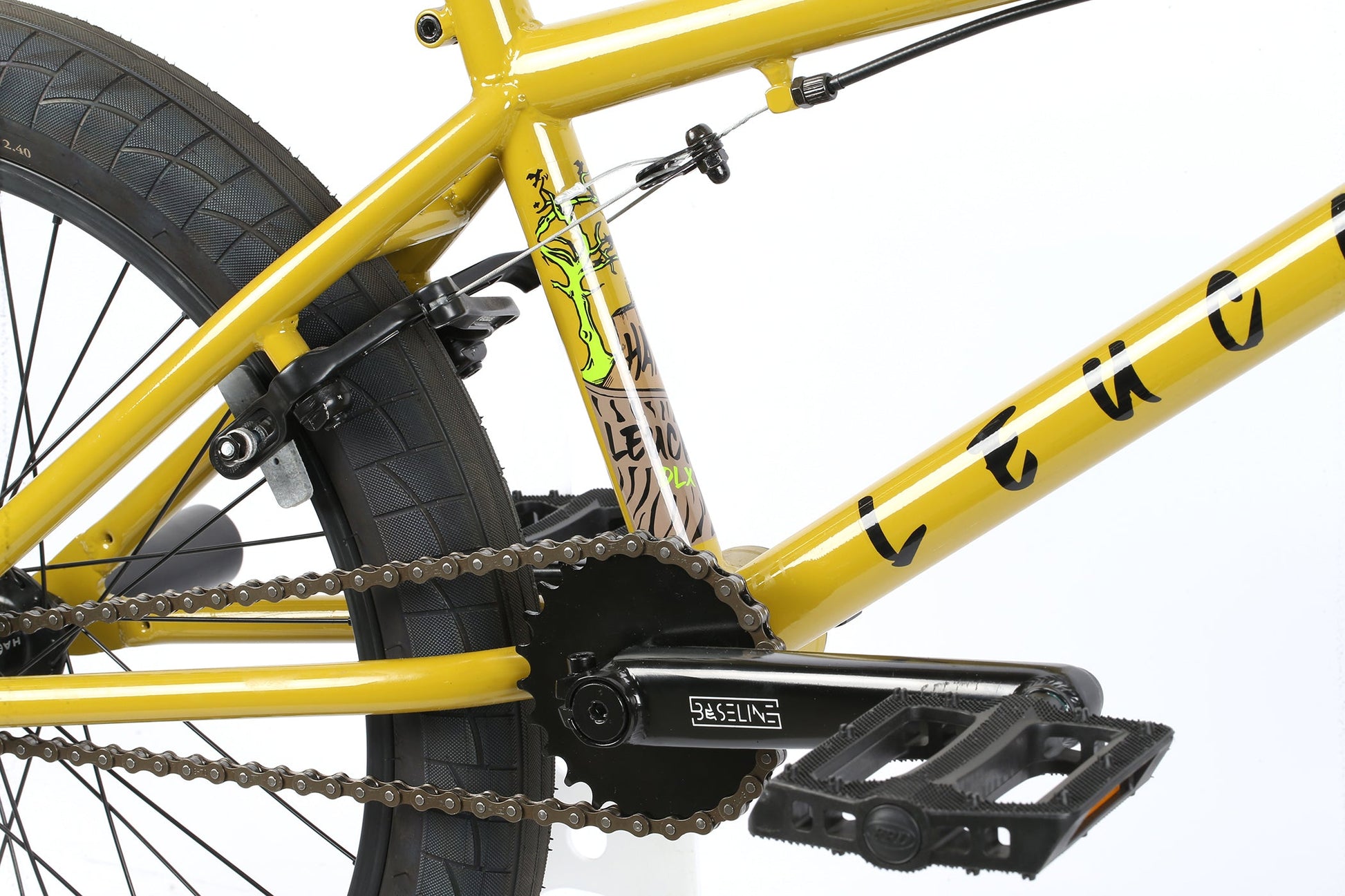 Close-up of a Haro Bikes Leucadia DLXs chain and Chromoly cranks, featuring thick tires and decorative patterns on the yellow frame near the wheel.