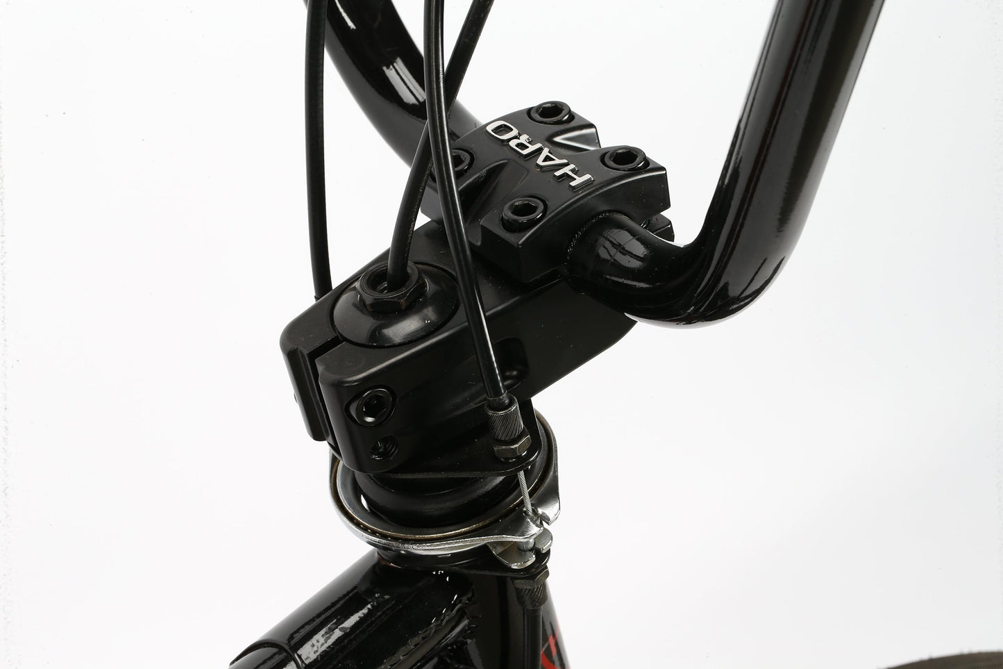 Close-up of a black handlebar with cables, a Haro Bikes stem, and part of the Leucadia DLX frame against a white background.