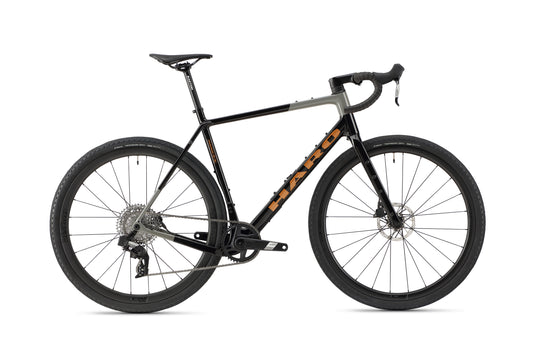 The Buzzard Carbon 2 by Haro Bikes is a sleek black and gray gravel bike with large tires, a drop-handlebar design, SRAM Apex disc brakes, and a visible rear gear mechanism. Its carbon frame features an orange logo, all set against a plain white background.