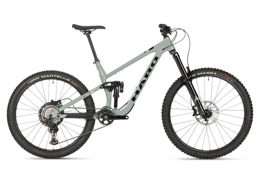 The Greer Alloy 1 by Haro Bikes is a green mountain bike with thick tires and a progressive suspension. It includes disc brakes, a black saddle, visible gears, and a sturdy alloy frame, ideal for rough terrains.