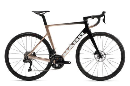 The Rivette Carbon 2 by Haro Bikes is a sleek, race-ready road bike featuring a gradient black to tan frame, high-pitch carbon fiber construction, drop handlebars, disc brakes, thin tires, and internal cable routing for speed and efficiency.