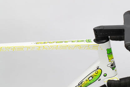 Close-up of a Haro Bikes Rivette Carbon LTD top tube, featuring a custom white paint job with vibrant green and yellow abstract graphics. RIVETTE appears in stylized letters. This Mark Ward design is part of the limited edition series. Handlebars are visible on the right.