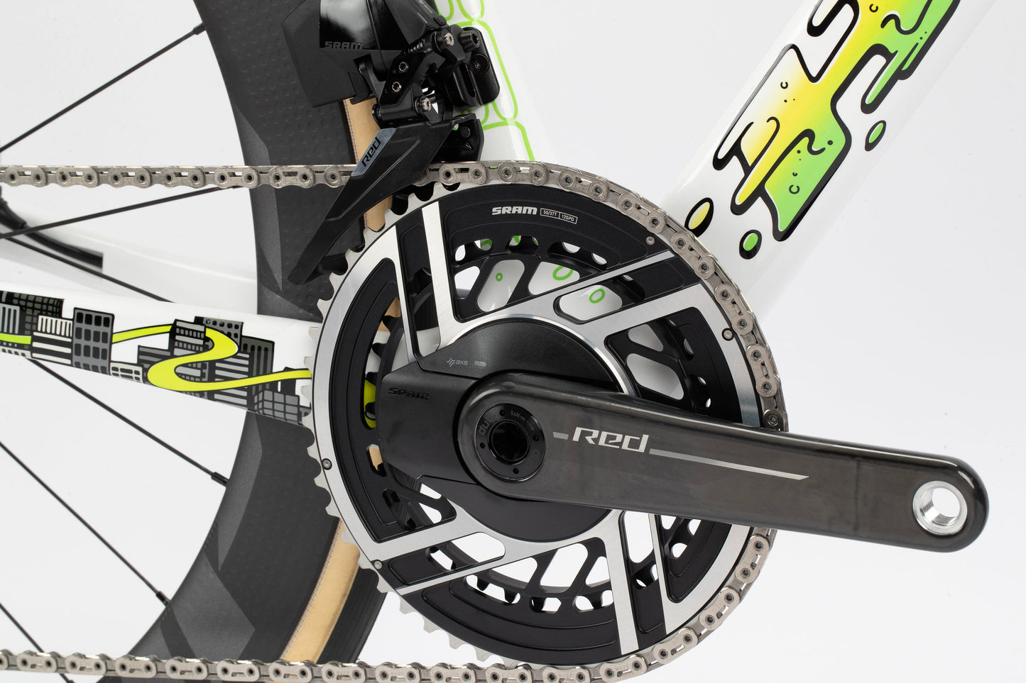 Close-up of a Haro Bikes Rivette Carbon LTD road bikes crankset and chainring. It features a black SRAM Red crank arm on a frame with white and green patterns. The rear wheel shows a grid design, showcasing Mark Wards artistry in this limited edition.