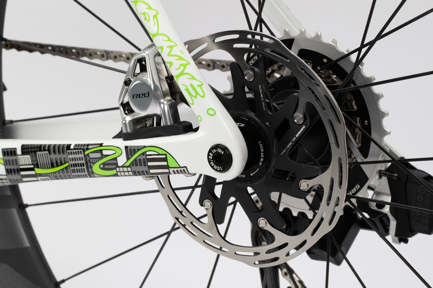 Close-up of a Haro Bikes Rivette Carbon LTDs rear disc brake and gear mechanism, featuring a silver and black rotor, chain, and part of the white frame with green and black graphics. This limited edition model exemplifies precision in every detail.