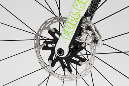 Close-up of a Haro Bikes Rivette Carbon LTD front wheel features a disc brake with silver rotor, black hub, and intricate spokes. The white fork, adorned with green text, highlights the precision synonymous with Mark Ward in this limited edition image.