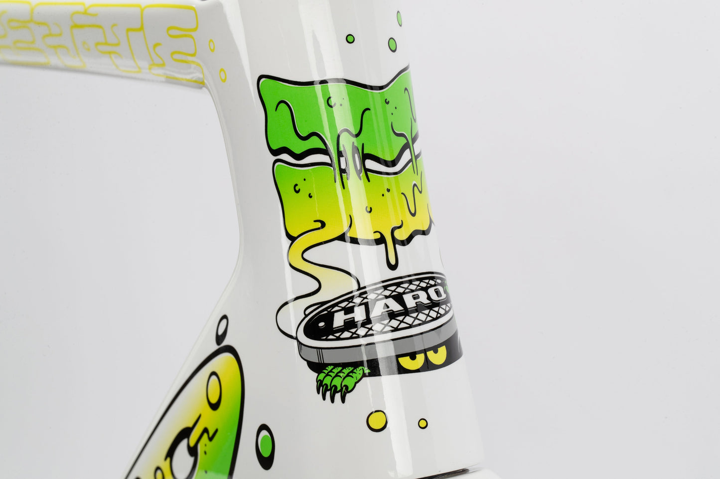 Close-up of a Haro Bikes Rivette Carbon LTD frame featuring vibrant graffiti-style artwork by Mark Ward. The design includes green and yellow drips, stylized faces, and the word HARO on a round emblem, all set against a white background. This limited-edition piece truly stands out.