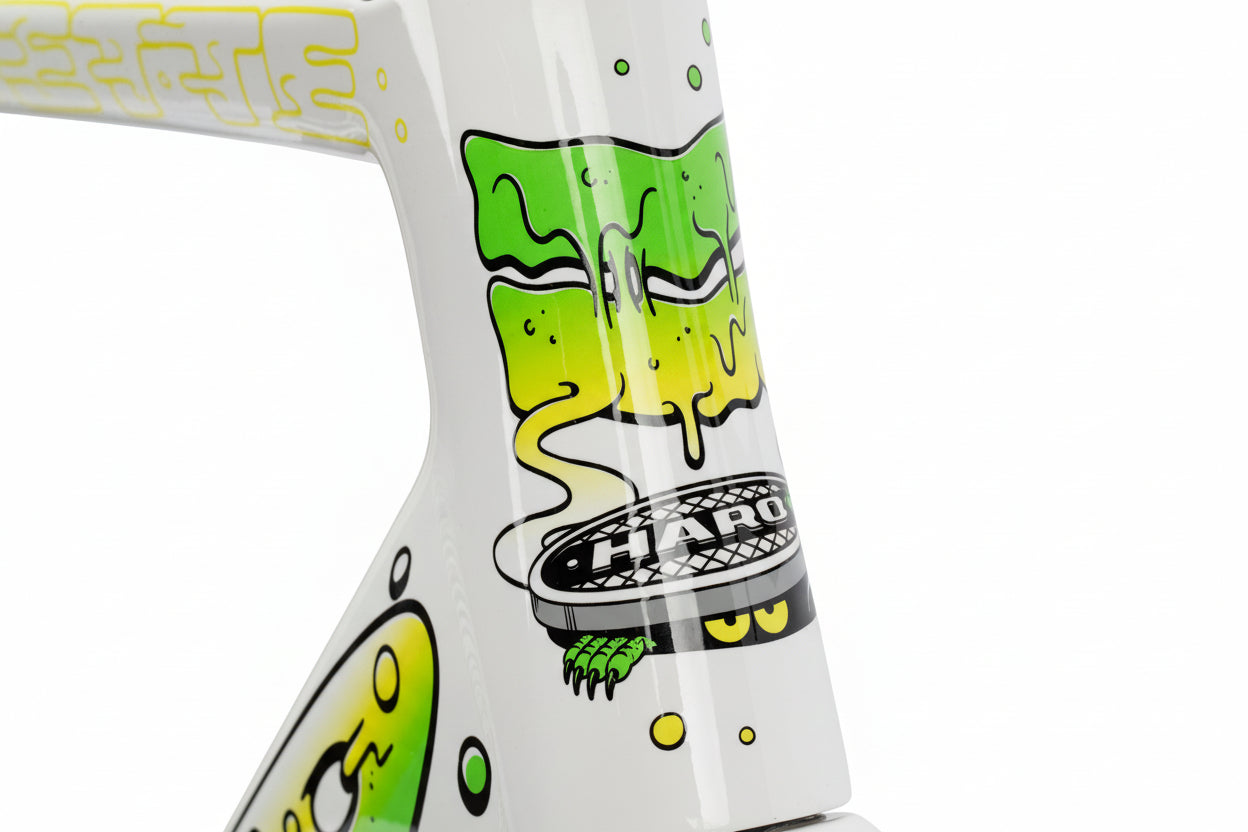 Close-up of a Haro Bikes Rivette Carbon LTD frame featuring vibrant graffiti-style artwork by Mark Ward. The design includes green and yellow drips, stylized faces, and the word HARO on a round emblem, all set against a white background. This limited-edition piece truly stands out.