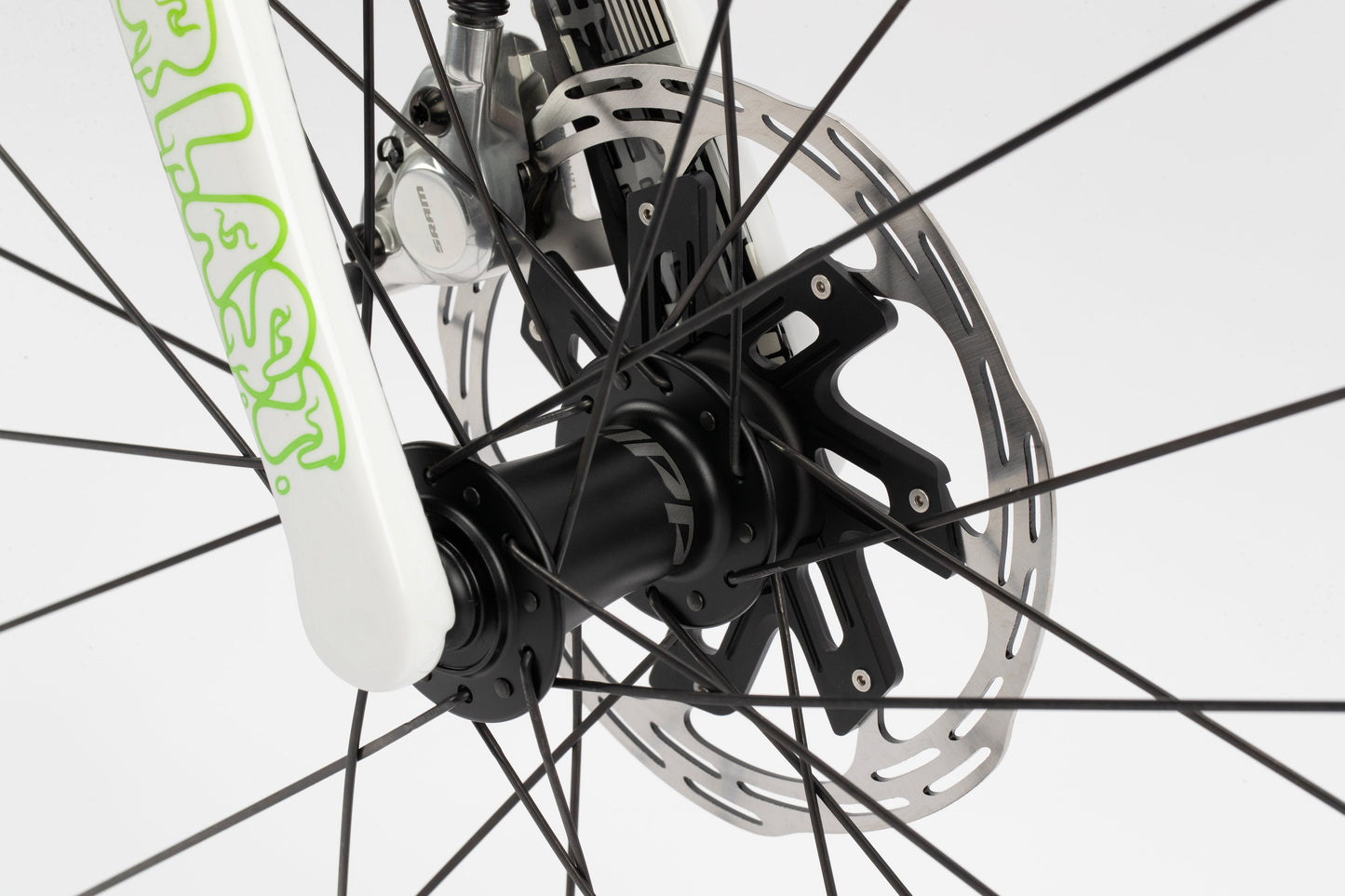 Close-up image of the front wheel of a Haro Bikes Rivette Carbon LTD, showcasing disc brakes, rotor, caliper, and spokes. Part of the bikes fork with green lettering is visible on the left against a plain white background.