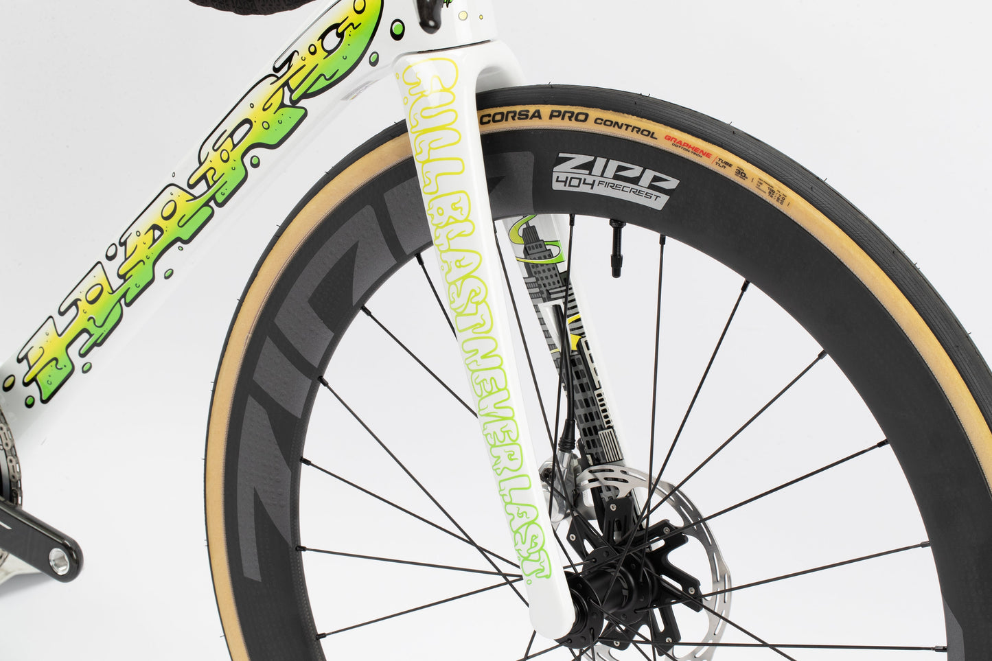 Close-up of a Haro Bikes Rivette Carbon LTD front wheel with a white fork featuring FULLBLAST NEVER LAST in neon green, lightweight ZIPP 404 wheel, Vittoria Corsa Pro Control tire, and a limited-edition frame by Mark Ward adorned with colorful graffiti-style designs.