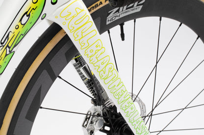 Close-up of a bicycle wheel featuring a custom fork design with vibrant graphics from the Haro Bikes Rivette Carbon LTD. WILLBLASTNEVERLAST is boldly displayed on the fork. The wheel includes a disc brake and spokes.