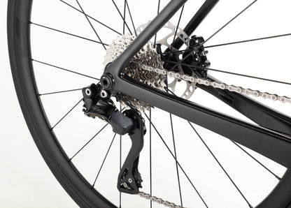 Close-up of the Rivette Carbon 2s rear wheel and gear system, showcasing the chain, cassette, and derailleur on a sleek black Haro Bikes frame with internal cable routing against a plain white background.