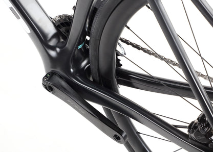 Close-up of the Rivette Carbon 2 by Haro Bikes reveals a black bicycle frame, emphasizing the rear triangle and crank arm. This road bike features sleek lines, internal cable routing, chainring detail, and part of the rear tire for a race-ready design.