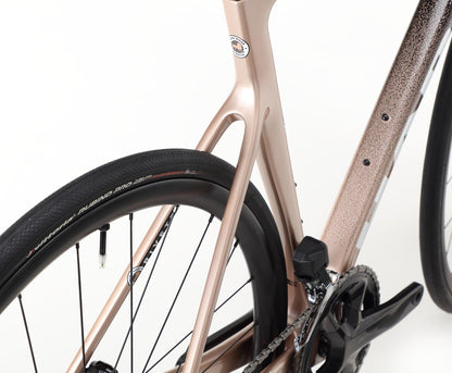 Close-up of the Haro Bikes Rivette Carbon 2, featuring a metallic rose gold frame with gradient details and internal cable routing, paired with a black wheel and detailed tread patterns.