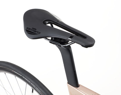 A Rivette Carbon 2 bike by Haro Bikes features a close-up of a black Selle San Marco saddle on a sleek seat post. Part of the race-ready road bike frame is visible, highlighting its modern minimalist design with internal cable routing against a plain white background.