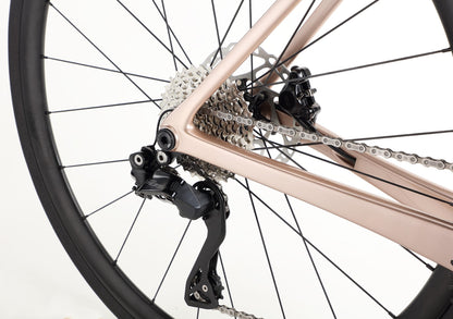 Close-up of a race-ready Haro Bikes Rivette Carbon 2 rear wheel and drivetrain, featuring a shiny metallic frame, gear cassette, chain, and derailleur on a plain white background. The components are clean and well-maintained.