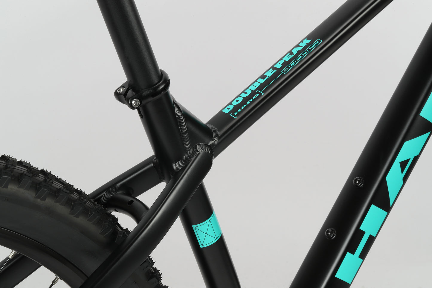 Close-up of the Double Peak 3 by Haro Bikes, featuring a black frame with turquoise text at the seat tube junction and rear tire area.