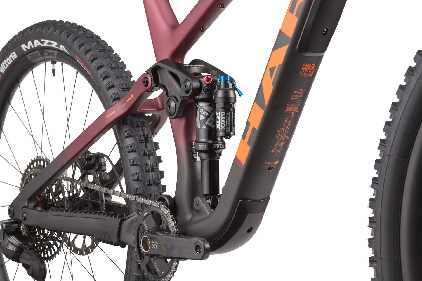 Close-up of the Daley Carbon 1’s rear suspension, chain, crankset, and carbon frame by Haro Bikes with orange and black graphics.