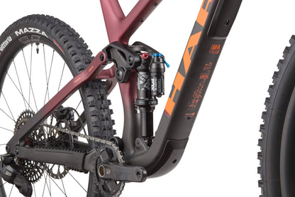 Close-up of the Daley Carbon 1’s rear suspension, chain, crankset, and carbon frame by Haro Bikes with orange and black graphics.