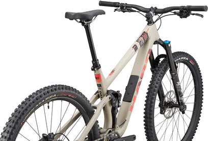 The Haro Bikes Daley Carbon 3 is a beige all-mountain carbon bike with red accents and thick knobby tires, seen from the rear side.