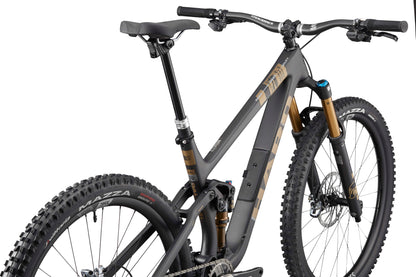 The Haro Bikes Daley Carbon Top Shelf is a matte gray, full-suspension carbon all-mountain bike with gold accents, shown from the rear.