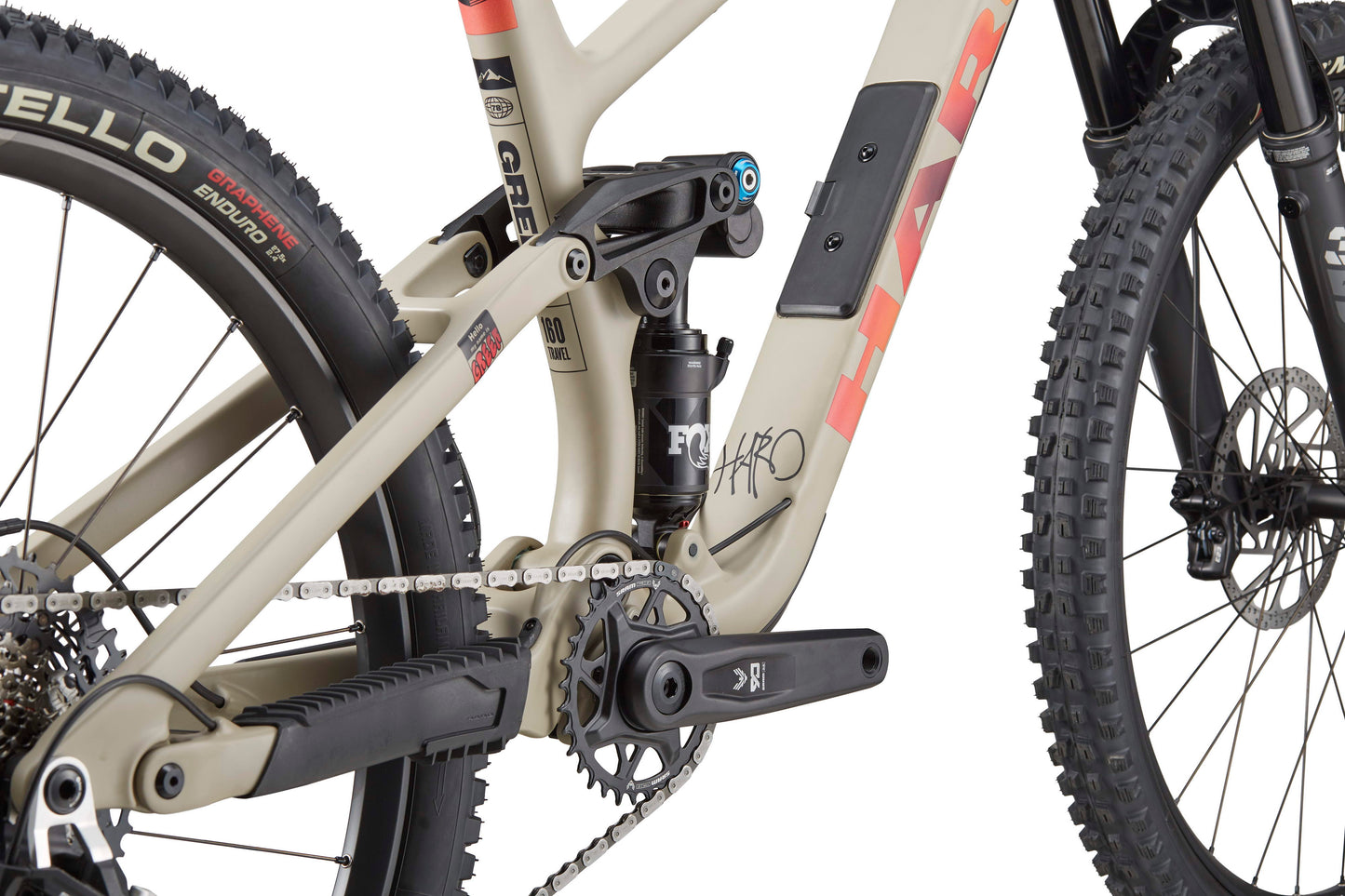Close-up of the Haro Bikes Greer Carbon 3 frame in beige and black, highlighting chain, pedals, suspension, and rear wheel for top downhill performance.