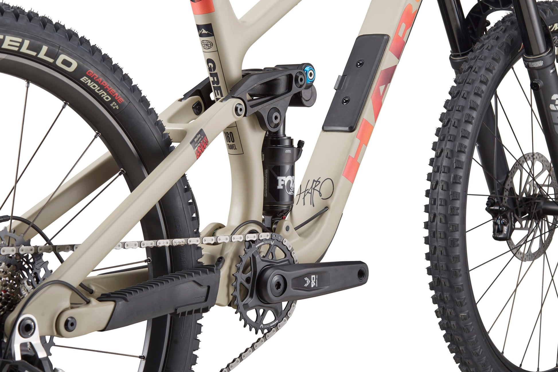 Close-up of the Haro Bikes Greer Carbon 3 frame in beige and black, highlighting chain, pedals, suspension, and rear wheel for top downhill performance.