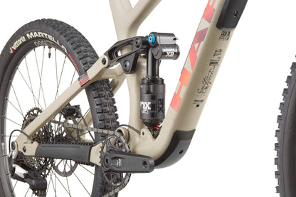 Close-up of Haro Bikes Greer Carbon 3’s rear suspension, drivetrain, and wheel on a beige frame with red graphics for trail agility.