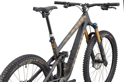 A Haro Bikes Greer Carbon Top Shelf mountain bike with wide knobby tires, black-gold frame, and Fox 38-Float-Factory fork.