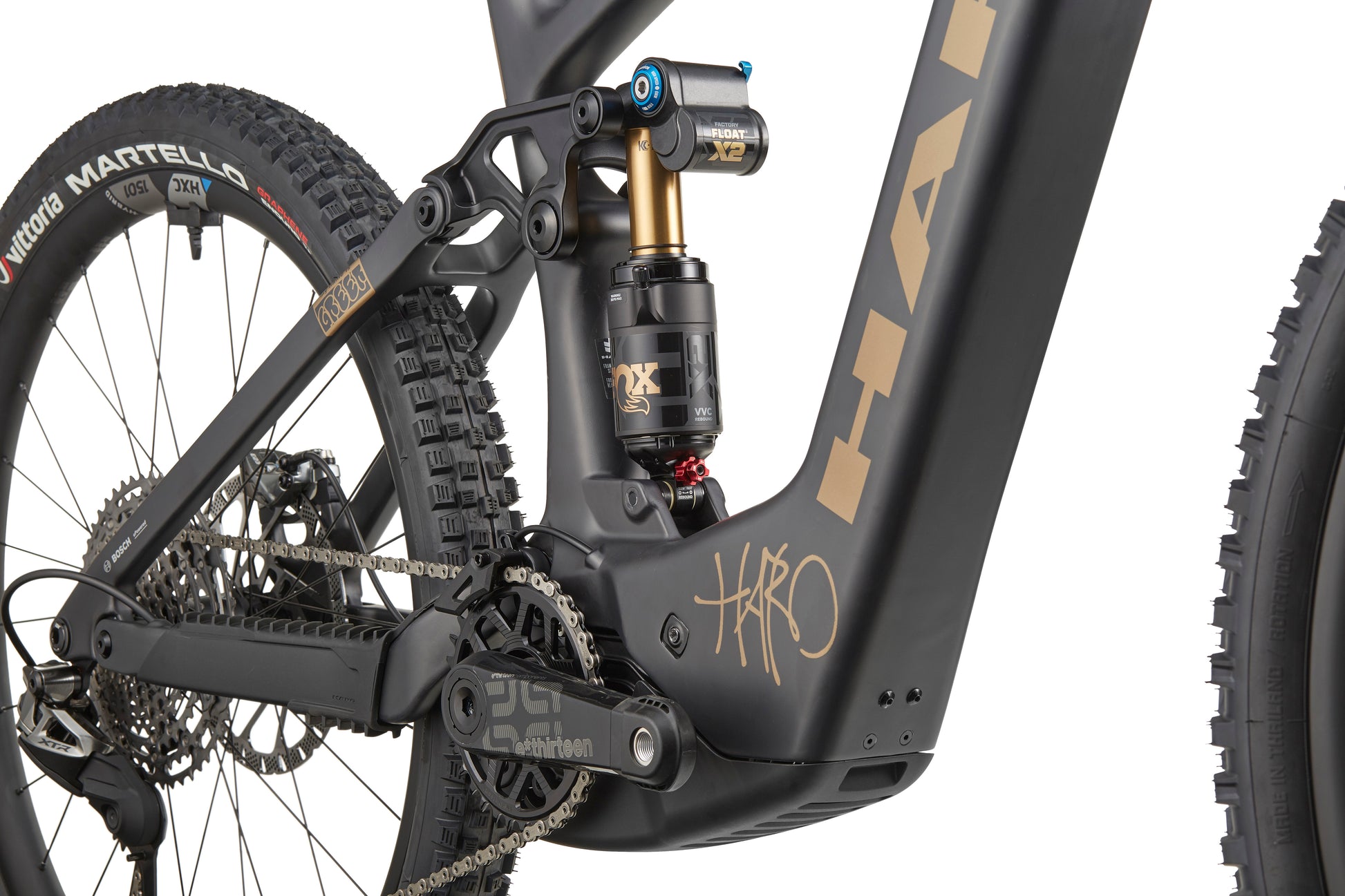 Close-up of a Haro Bikes eGreer Carbon Top Shelf E-Bike's rear suspension, drivetrain, and tire on matte black carbon frame with Bosch CX.