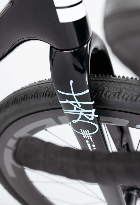 Close-up of the Haro Bikes Buzzard Carbon Frameset “Black Sunrise” fork, with white accents, textured tire, and partial handlebar visible.