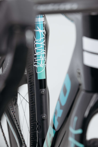 Close-up of a Haro Bikes Buzzard Carbon Frameset “Black Sunrise” with teal and white graphics, featuring the front suspension fork.