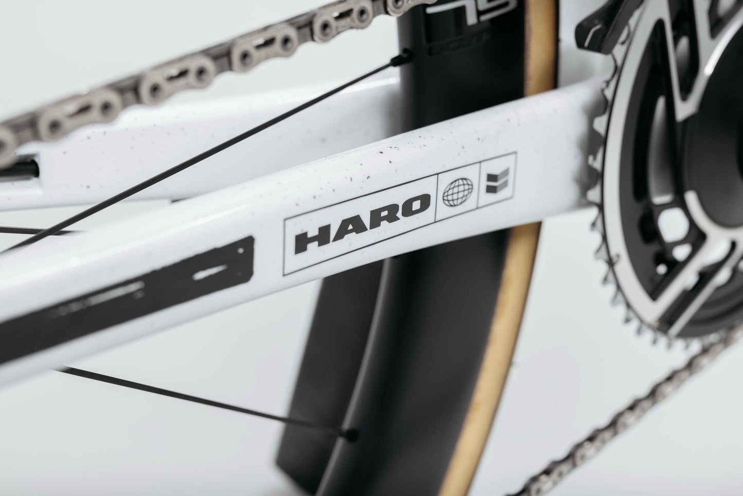 Close-up of a white Haro Bikes frame, chain, gear, tire, and Partimos Carbon Custom "Black Sheep" details visible.