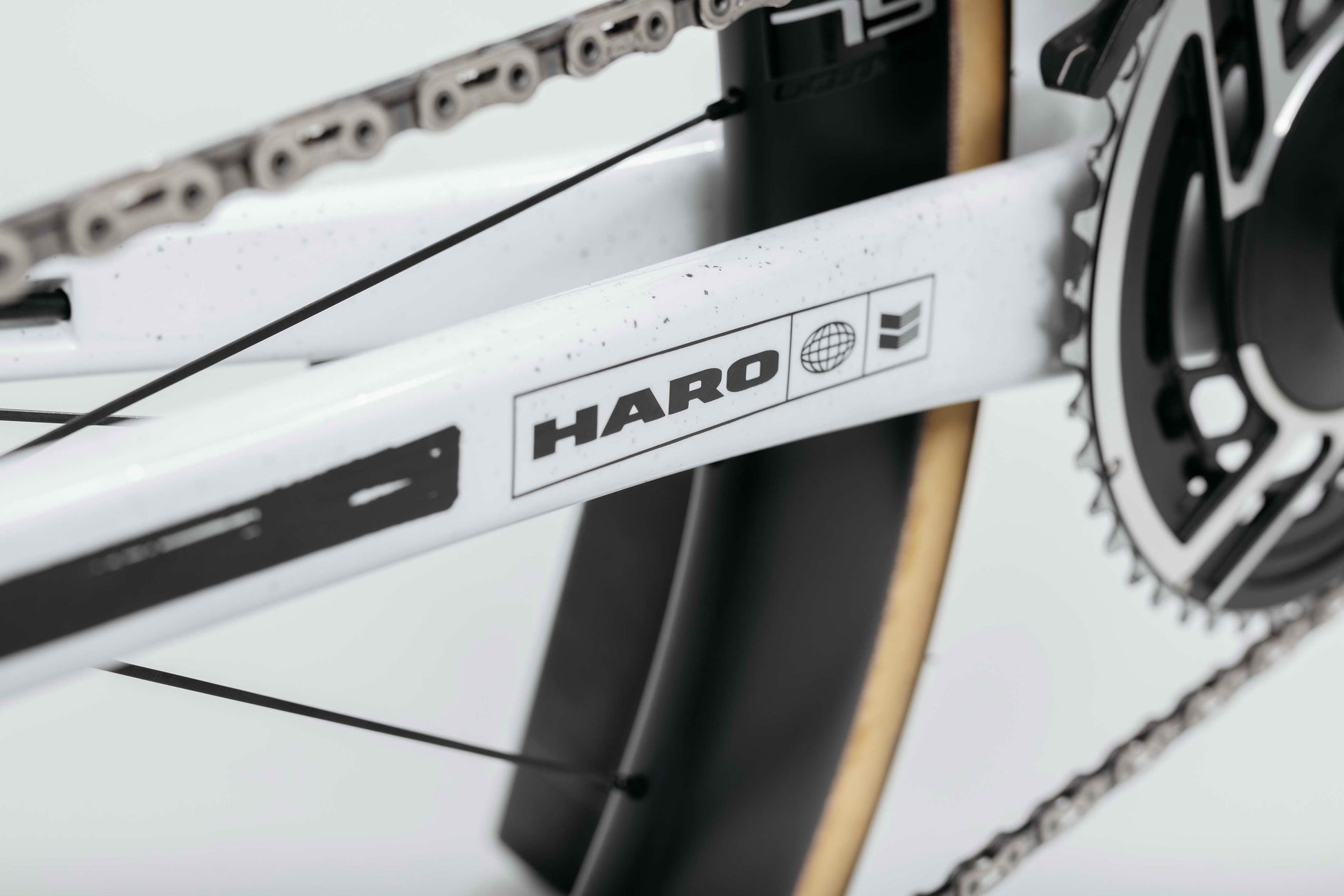 Close-up of a white Haro Bikes frame, chain, gear, tire, and Partimos Carbon Custom "Black Sheep" details visible.
