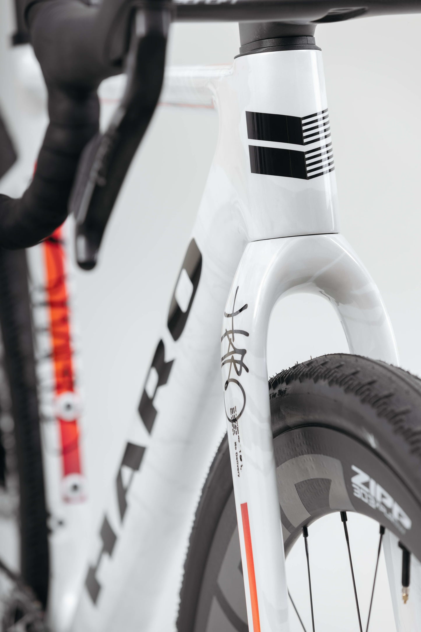 Close-up of a white Haro Bikes Buzzard Carbon Custom “Desert Sunset” front frame, featuring handlebars, Zipp tire, and black decals.