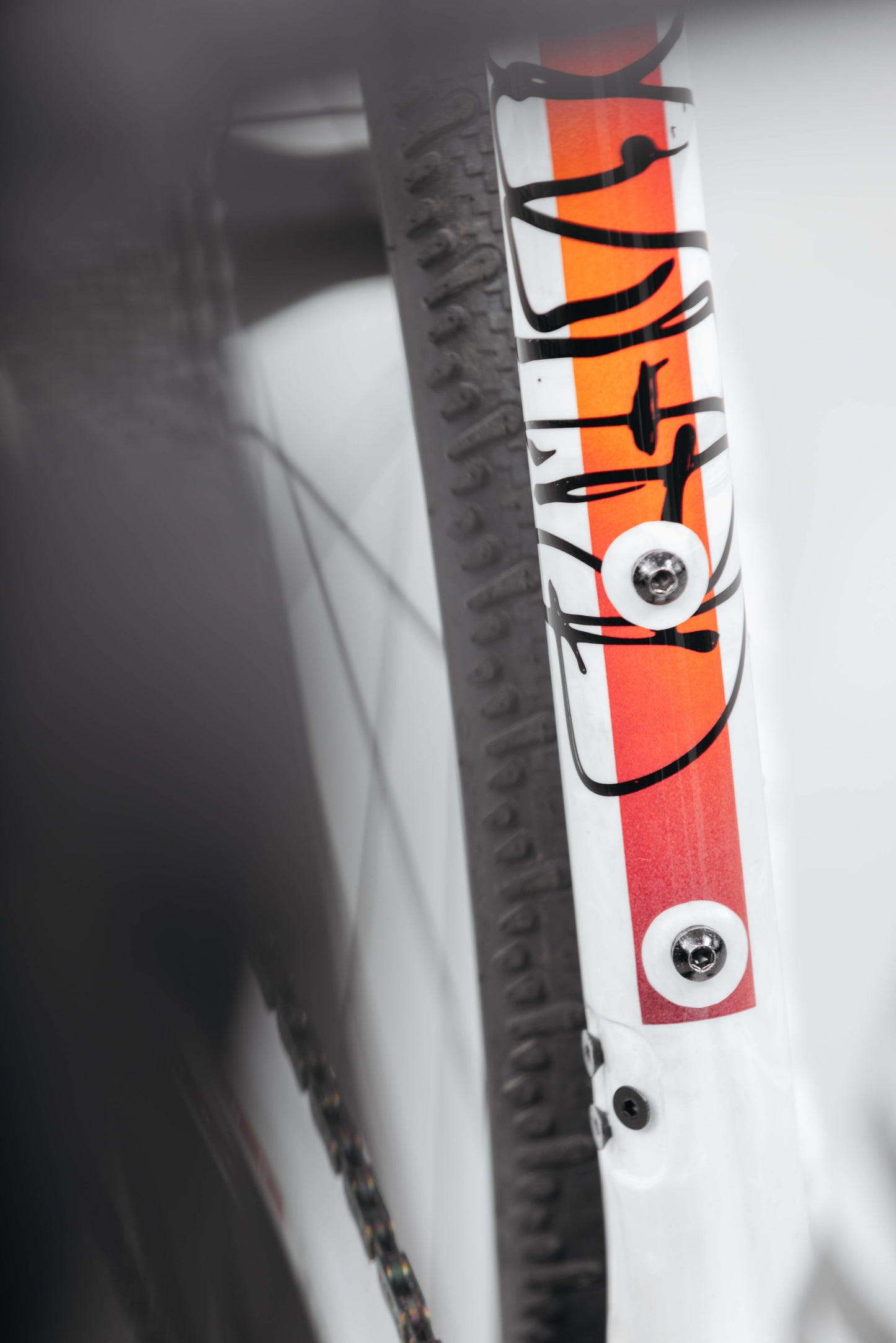 Close-up of a Haro Bikes Buzzard Carbon Custom “Desert Sunset” gravel frame, with orange/white stripes and black text, next to a tire.