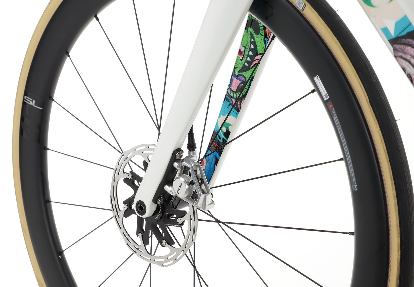 Close-up of a Haro Bikes Rivette Carbon EP Edition wheel: patterned fork, disc brake, white frame, tan tire pairs with black rim.