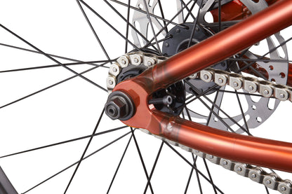 Close-up of a HARO Steel Reserve TS rear wheel with spokes, chain, disc brake, and orange frame on a white background.