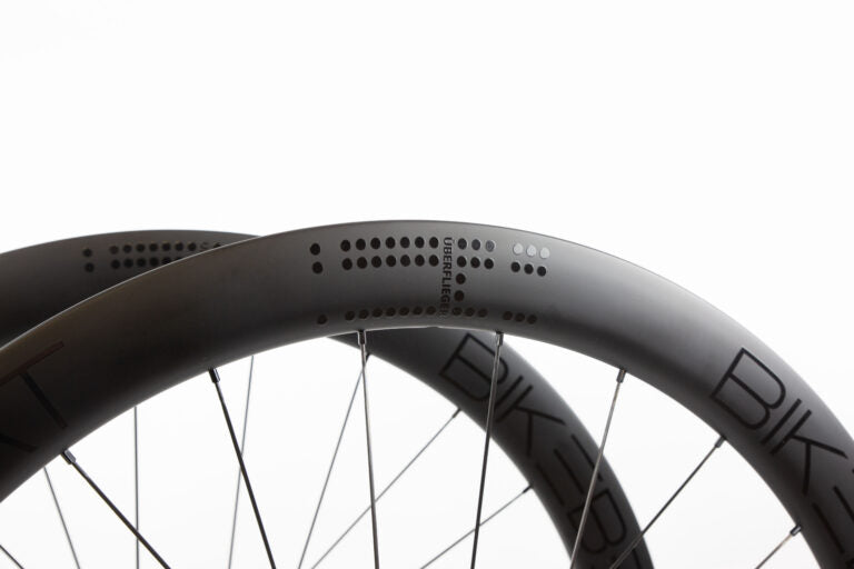 Close-up of two carbon fiber Bike Beat Überflieger Pro 50 Disc wheels featuring dot patterns and text on the rims.