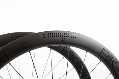 Close-up of two carbon fiber Bike Beat Überflieger Pro 50 Disc wheels featuring dot patterns and text on the rims.